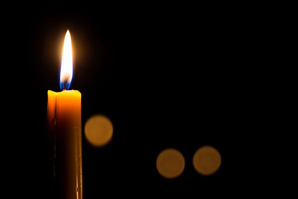 Single tall lit candle with a black background