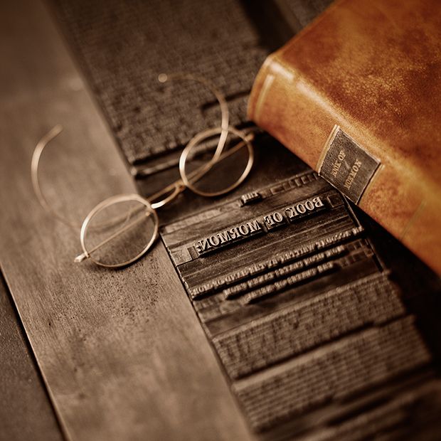 An old copy of the Book of Mormon sitting on a printing press, it is another testament of the gospel of Jesus Christ.