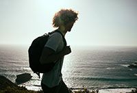 Young man with a backpack looking out at the ocean.