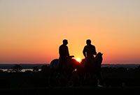 Silhouettes of two men riding horseback, talking with one another.