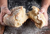 A baker's hands holding a broken loaf of bread.