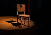 A lone chair lit on a stage.