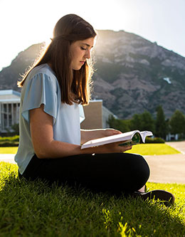 A young woman studying on BYU campus with Y mountain in the background