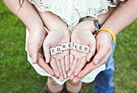Two hands cupped in a heart shape, holding letter tiles that spell out the word "forever"