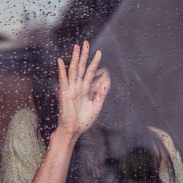 Sad woman pressing her hand up against the inside of a window.